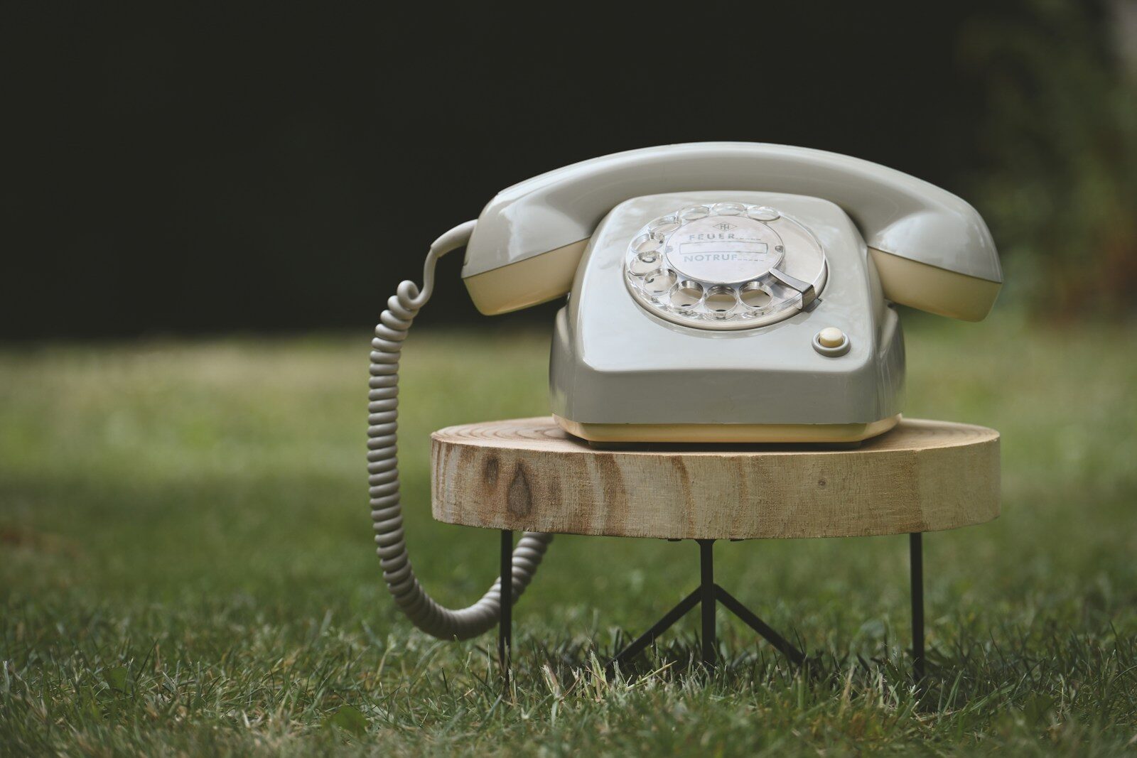 Old rotary telephone on a wooden stool in green grass
